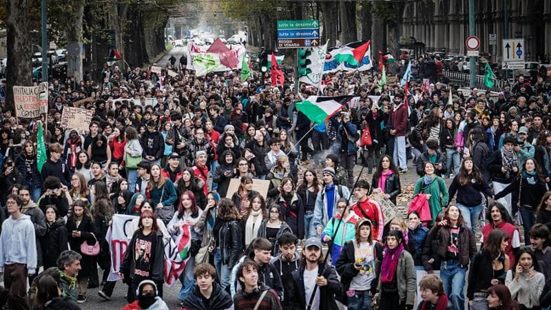 Corteo di persone con bandiere lungo una strada cittadina